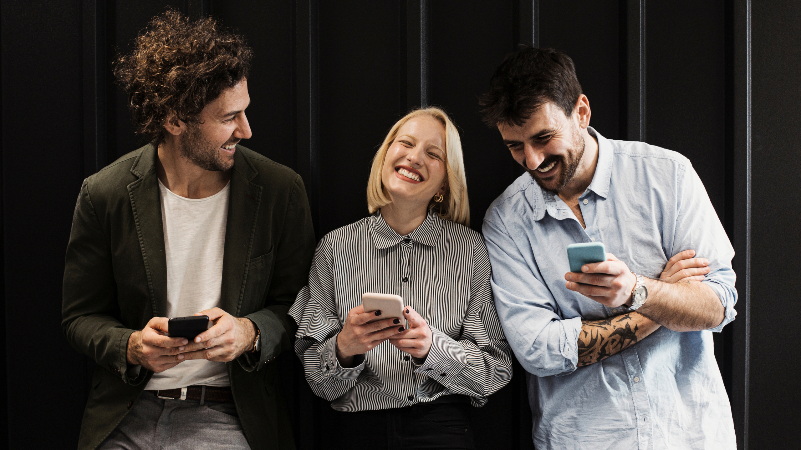 Drei lächelnde Personen stehen nebeneinander und schauen auf ihre Smartphones